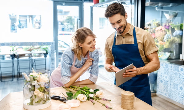 Young florists in aprons using digital tablet while working together